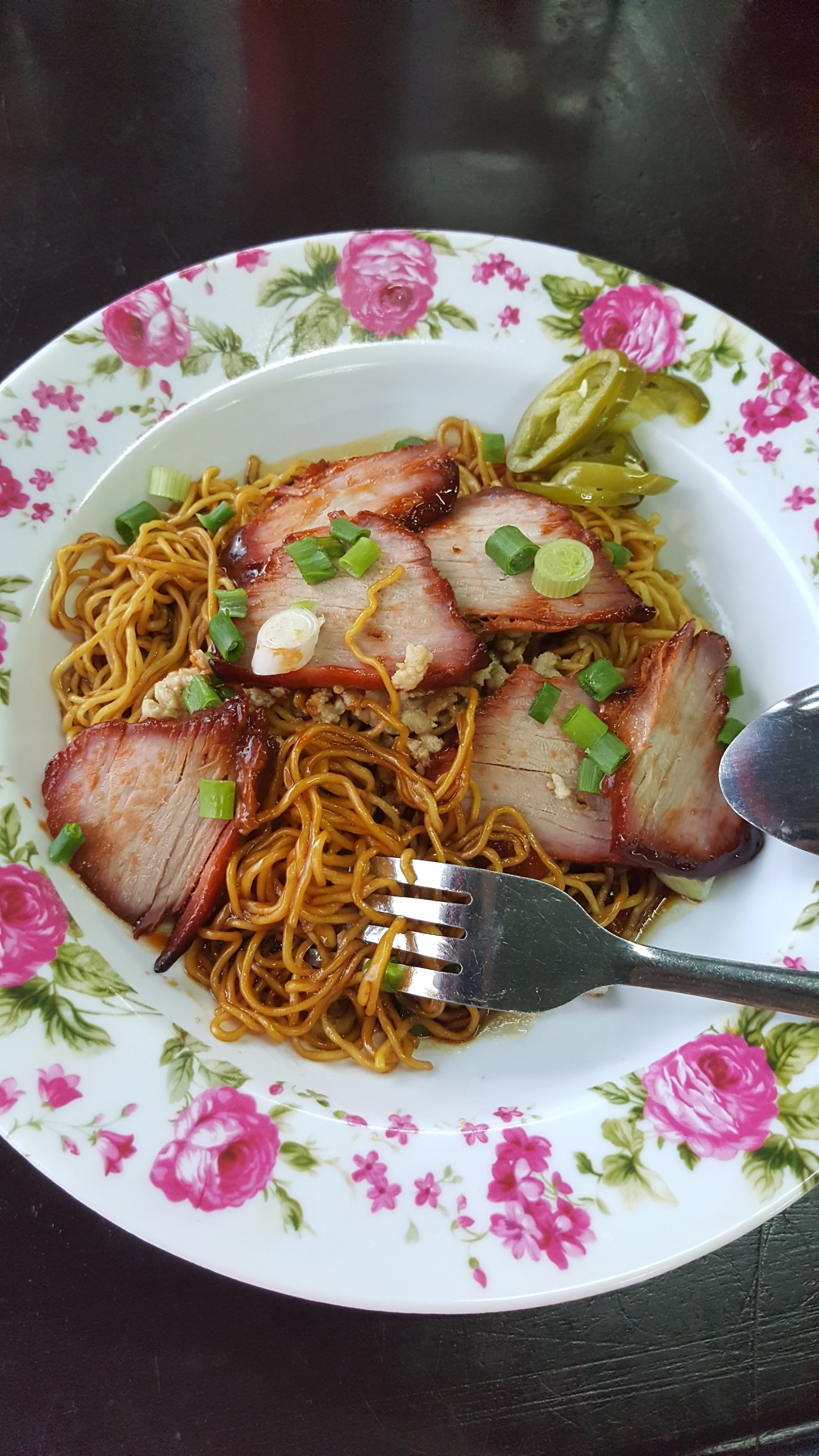 A dish with a rim of painted, pink flowers filled with Cantonese duck noodles: slices of red duck on top of dark noodles