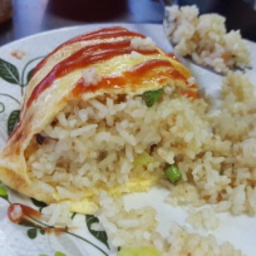 A plate with an omelet cut in half. Inside of the omelet is Chinese fried rice. On top of the omelet are decorative lines of katchup