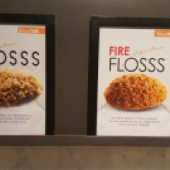 Two signs side by side. One says "Signature Flosss" (with three Ss) and has a picture of a pile of light, flaky stuff. The other sign says "Signature Fire Flosss" and has a picture of flacky red stuff